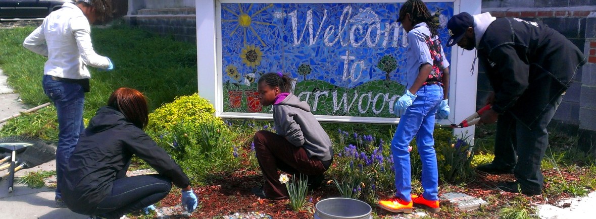 A group of residents planting flowers around the "Welcome to Harwood Sign".